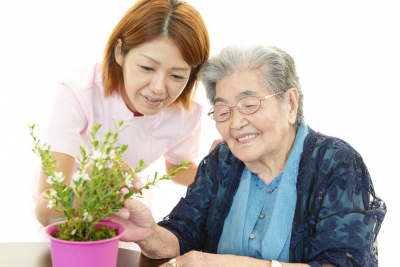 smiling senior woman and caregiver looking at the plant